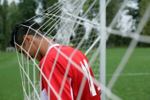A soccer player stands with his head tangled in a goal net, expressing playfulness on the field.